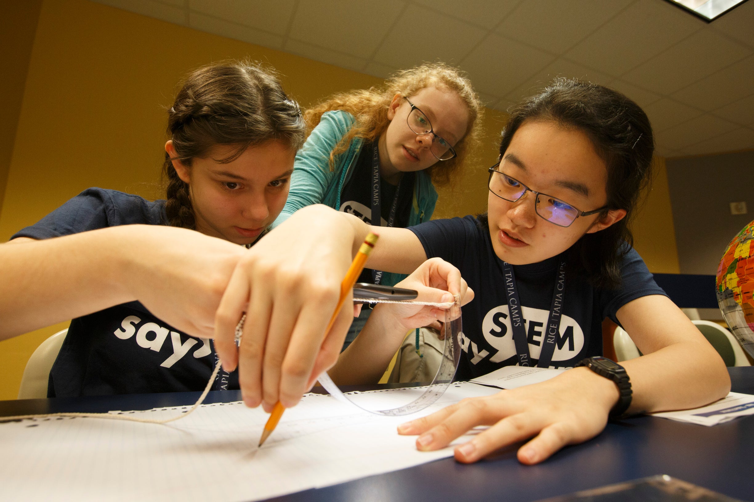 3 female campers working on a project and writing on the same paper.