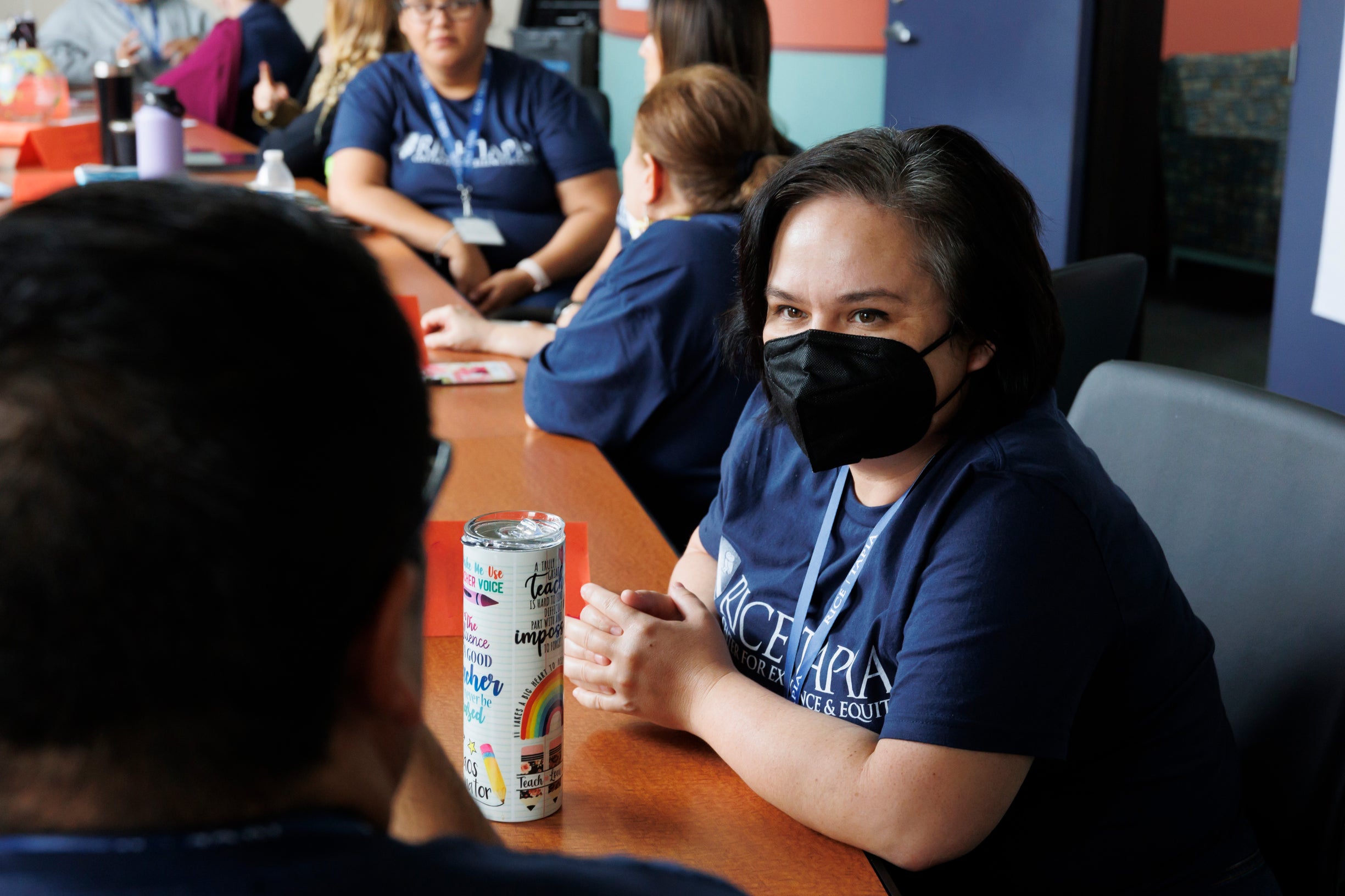 Educator wearing a face mask is looking at another educator while in discussion with others.