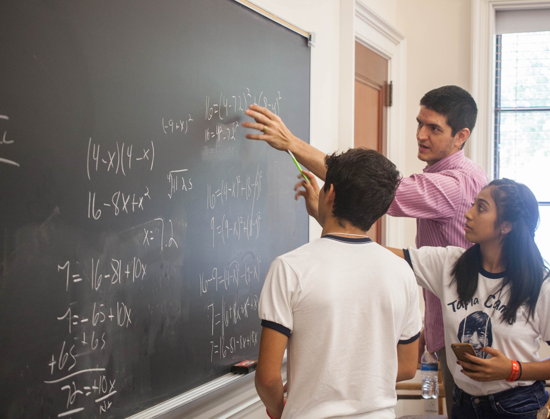 Two campers with Rice professor doing math on a chalkboard.
