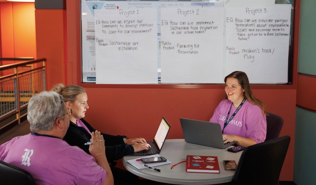 3 educators sit around a table discussing their projects